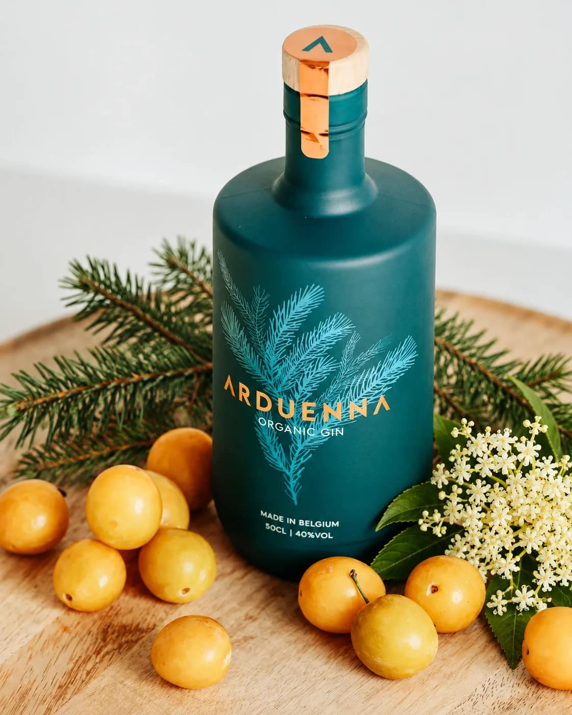 Bouteille Arduenna entourée de sapin, de mirabelles et de fleur de sureau