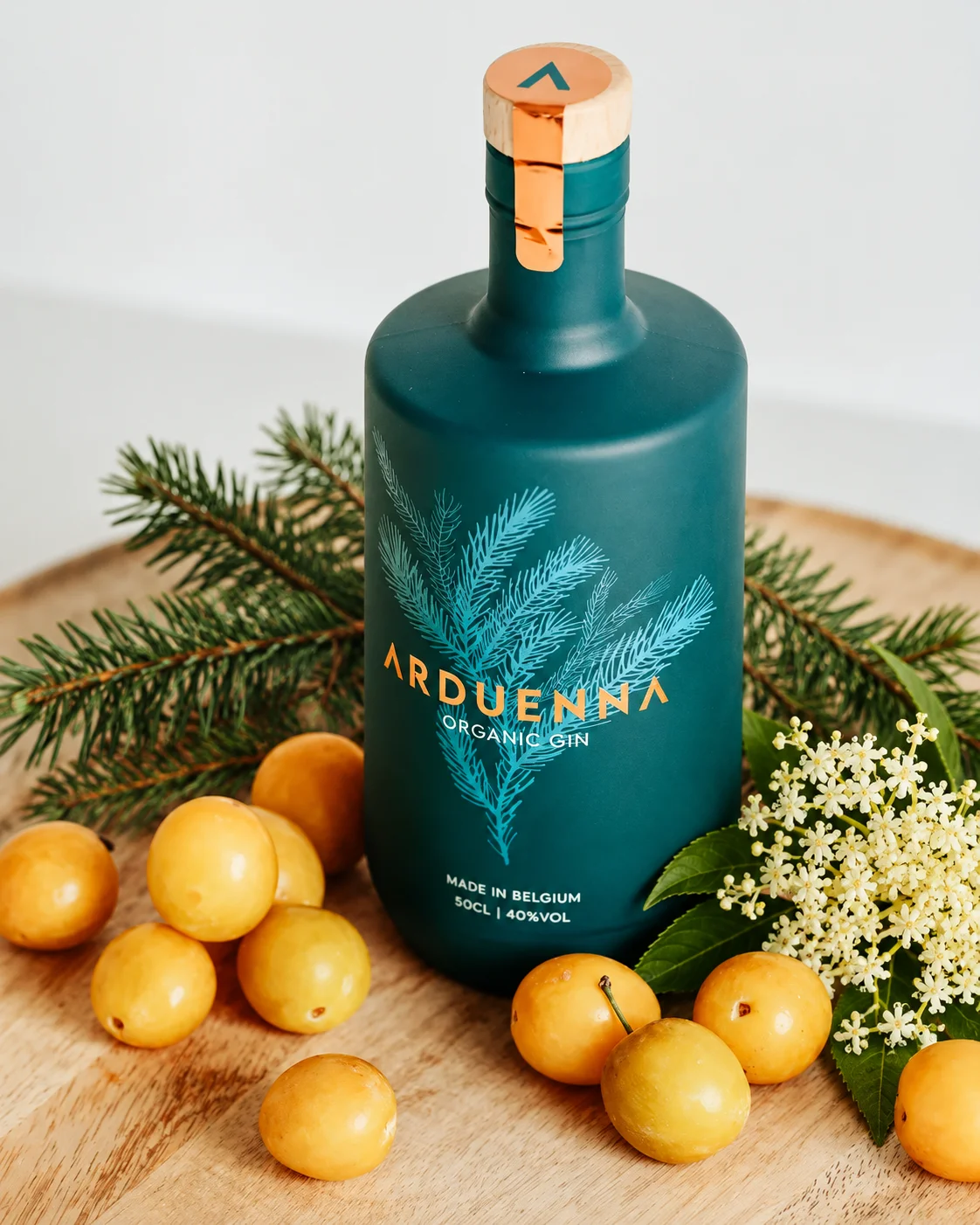 Bouteille Arduenna entourée de sapin, de mirabelles et de fleur de sureau